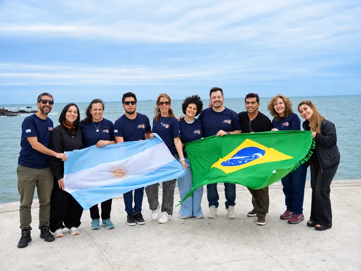 El equipo comparte una fotografía con las banderas frente al mar.
